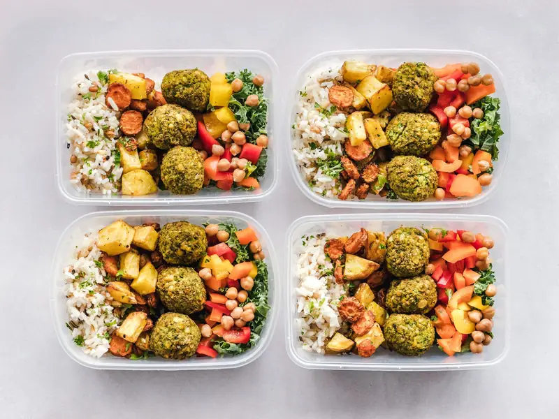 Quatro marmitas iguais com arroz, falafel, legumes assados e grão-de-bico, vistas de cima